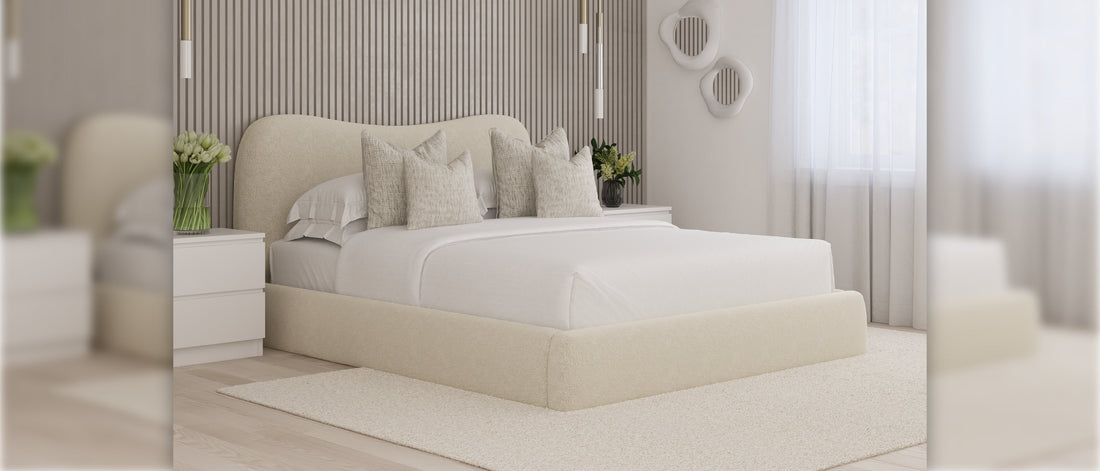 Cream upholstered king size ottoman storage bed with curved headboard, styled with neutral cushions in a modern bedroom with slatted wall panels and soft natural light