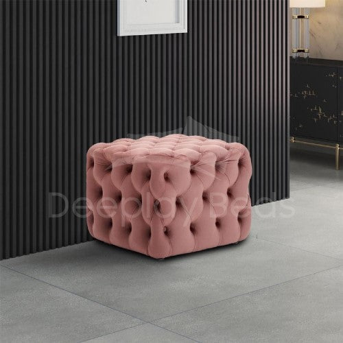 Pink tufted ottoman in a room with a black textured wall and gray floor.