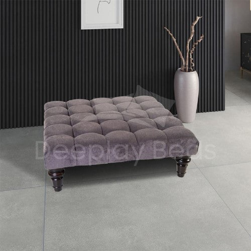 Gray tufted ottoman in a room with a vase and wall art.