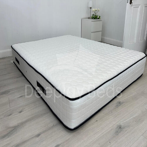 White mattress on a wooden floor with a nightstand in the background