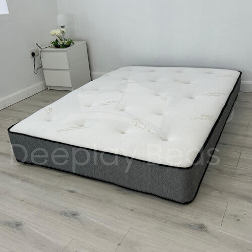 Gray and white mattress on a wooden floor with a nightstand in the background.