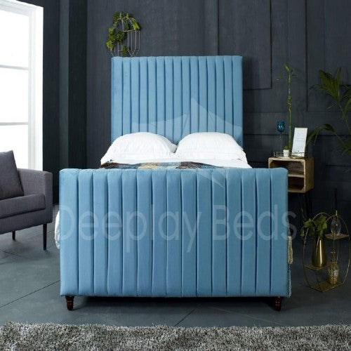 Blue upholstered bed in a room with a gray wall and a window.