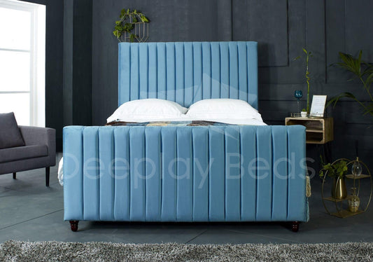 Blue upholstered bed in a bedroom setting with a gray sofa and side table.