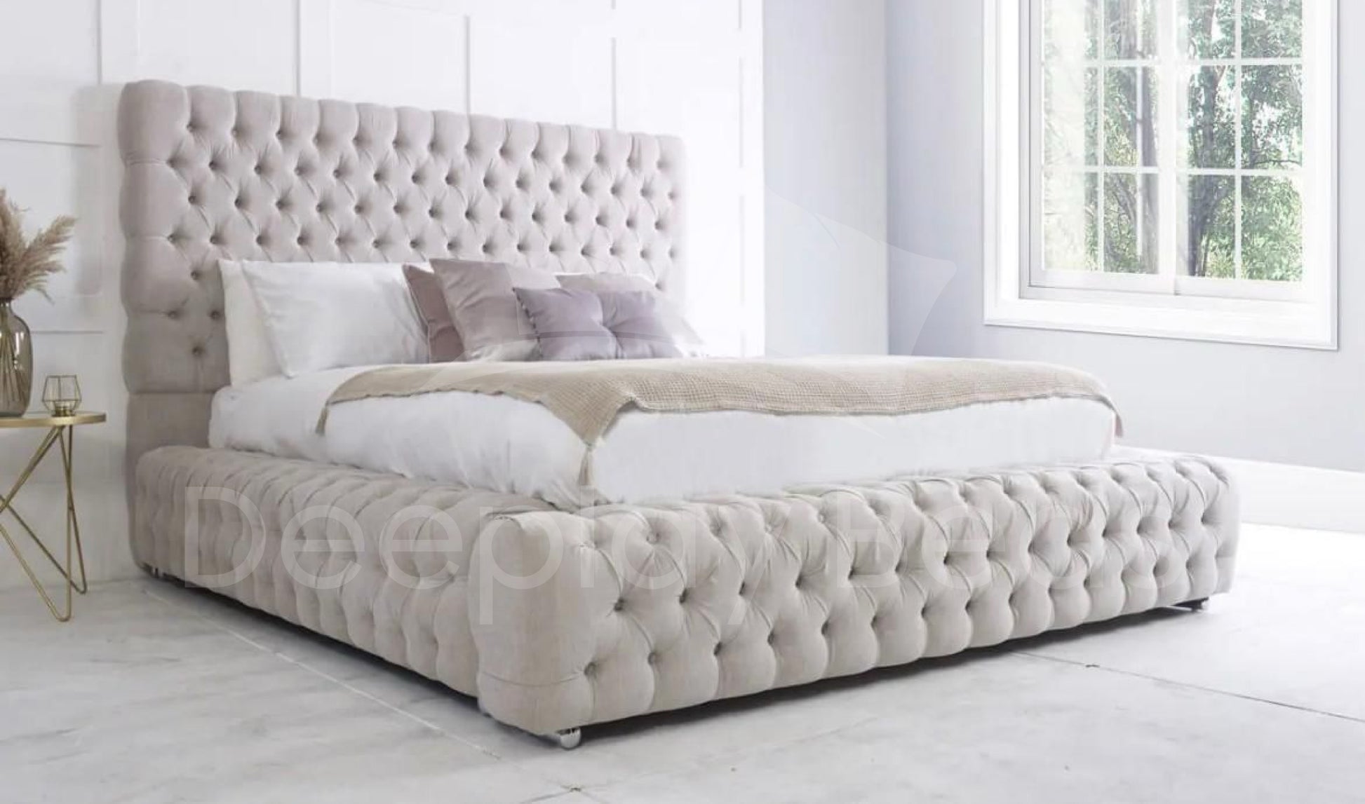 Beige tufted bed in a bedroom with white walls and a window.