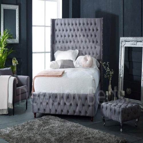 Gray tufted bed with matching headboard and ottoman in a bedroom setting.