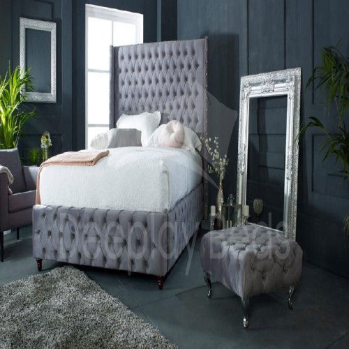 Gray tufted bed with matching headboard and ottoman in a bedroom setting.